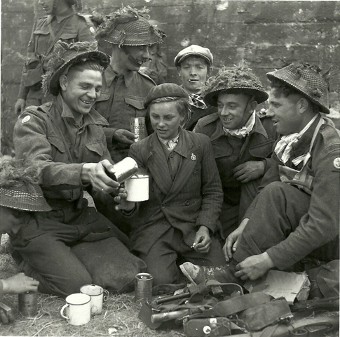 Groupe de sapeurs des Royal Engineers du 9th Beach Group avec un enfant qui goute à une boite de conserve "auto chauffante" de chocolat